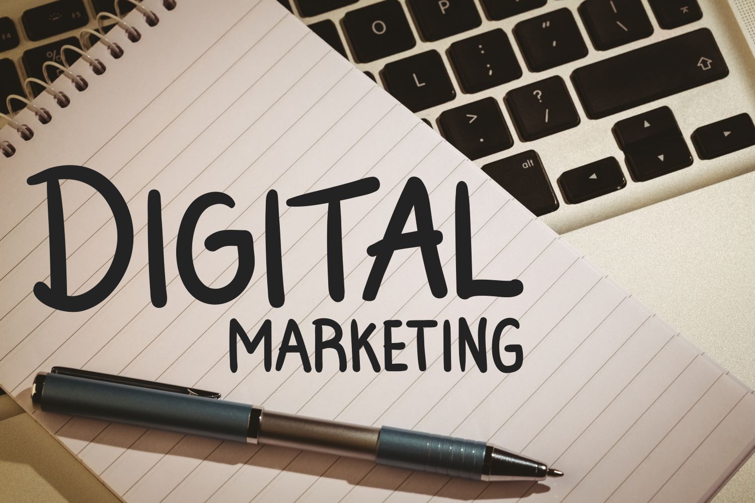 The words digital marketing is written on a notepad that sits on top of a laptop.